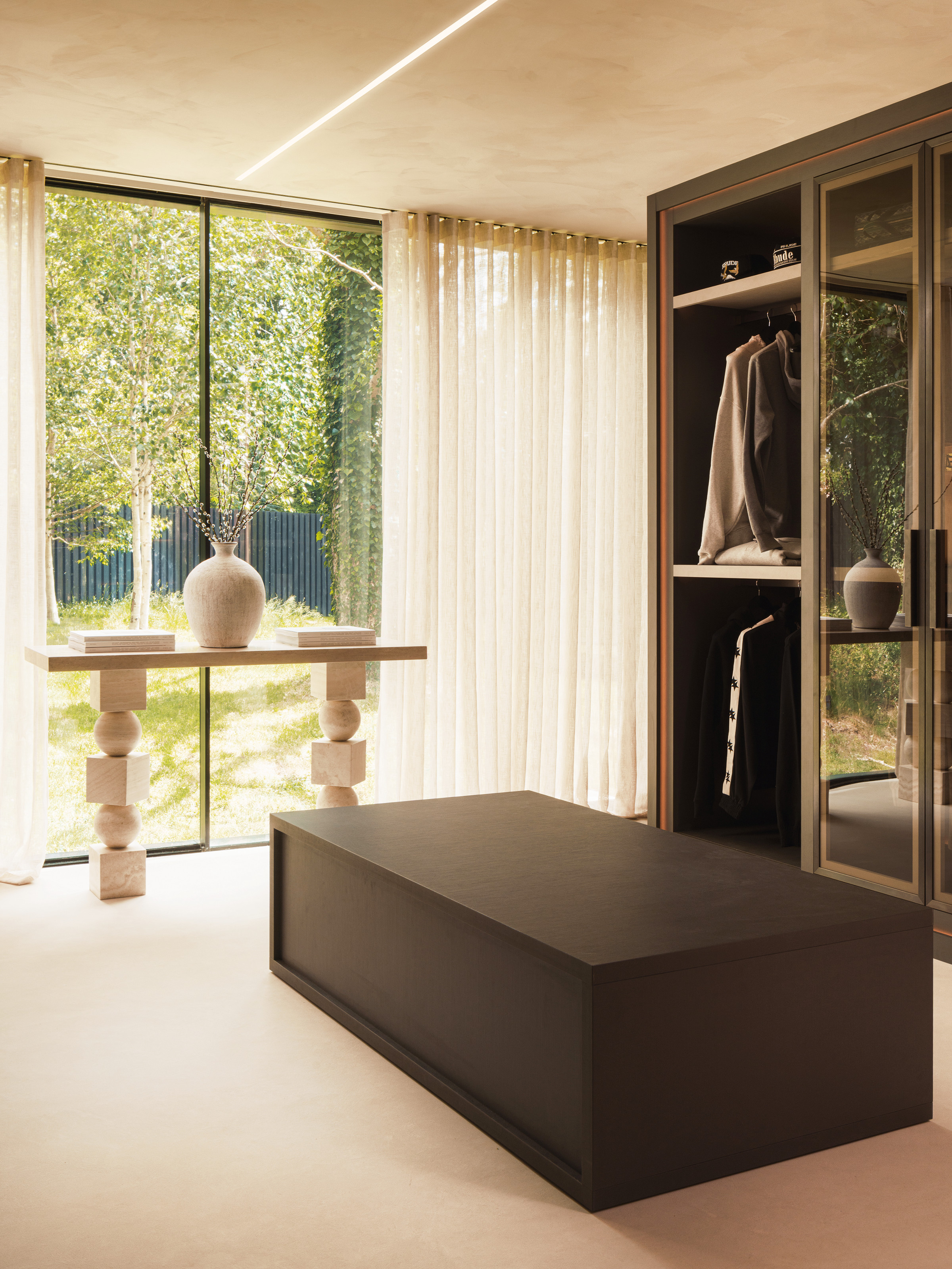 Dressing room with glazed wardrobe, black centre table/bench and sculptural beige console