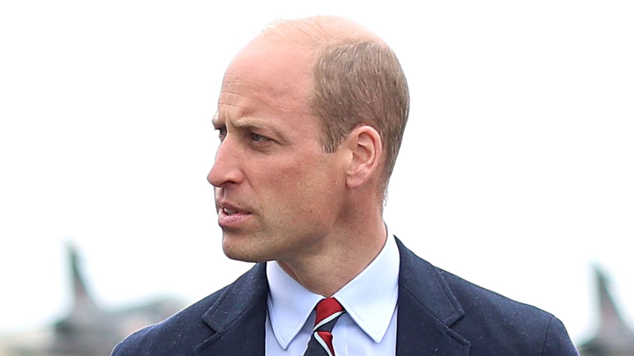 Prince William looks pensive while walking in front of service aircraft and wearing a suit with a striped tie