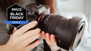 Hands holding a Sony camera and a Sony lens with a black Space.com Black Friday deals badge in the upper-left corner.