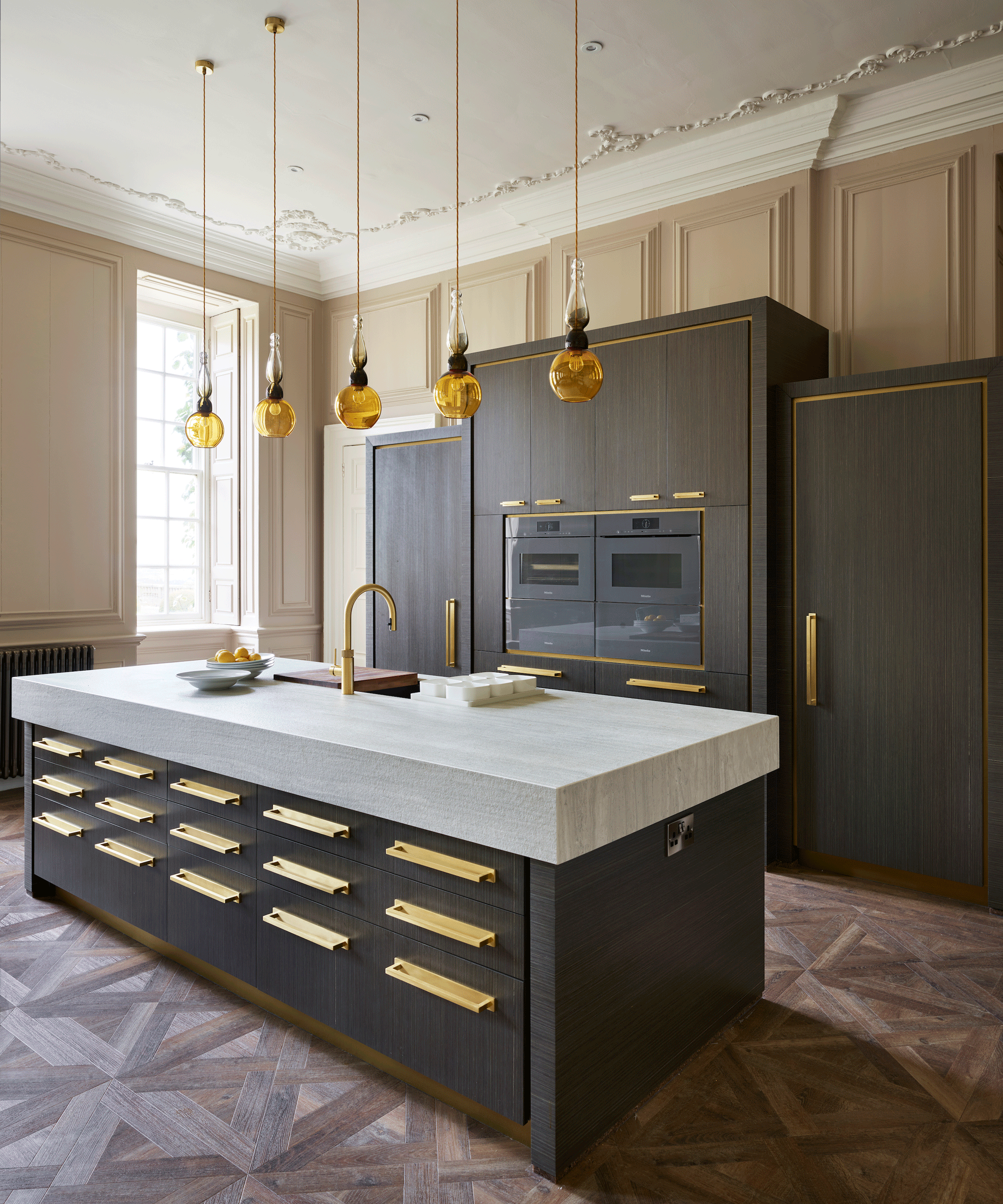 Large kitchen island with a thick stone worktop and gold hardware