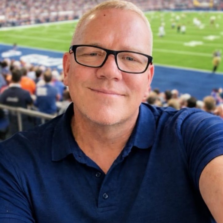 Smiling headshot of Andy Towers behind the end zone of an NFL game.