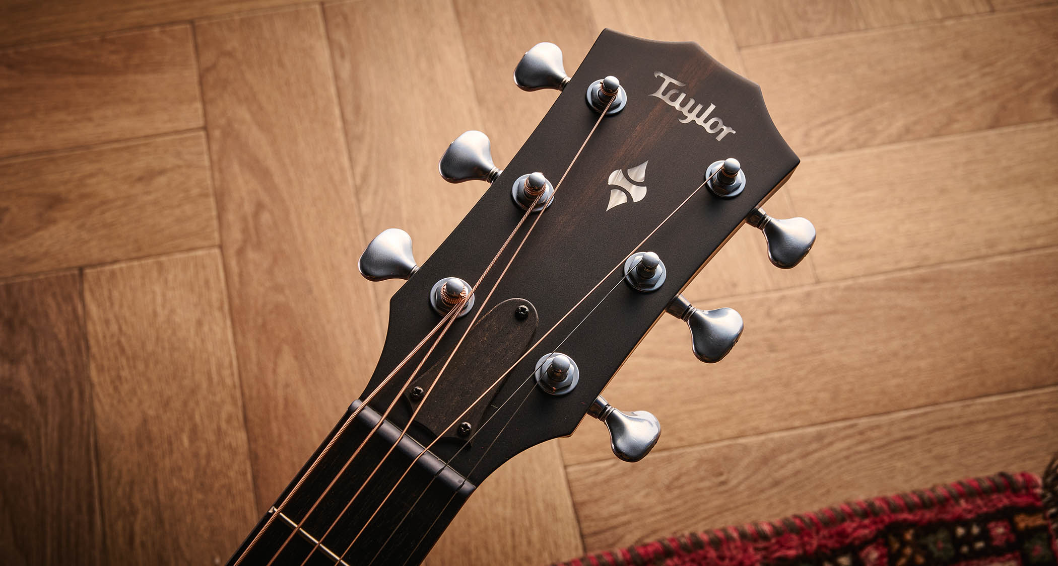 Taylor Builder’s Edition 514ce Kona Burst pictured against a wooden floor and patterned rug.