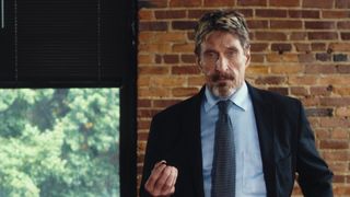 John McAfee posing in a suit against a brick wall