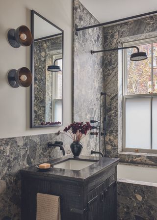 A dramatic dark stone bathroom featuring wall light fittings and stone covered walls