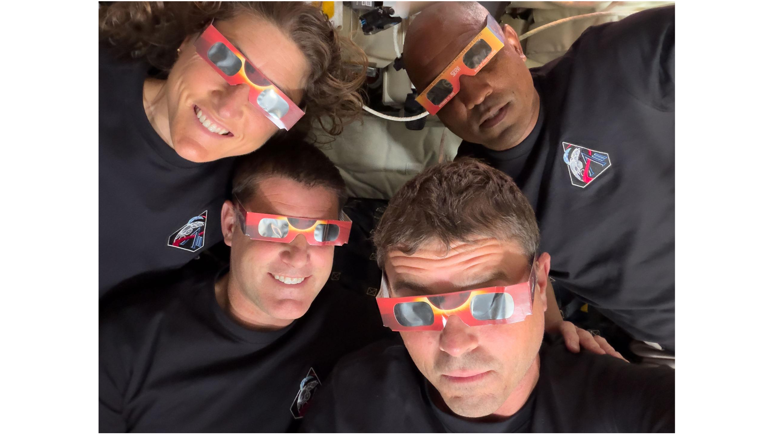 closeup of four people wearing reflective solar-eclipse glasses inside a spacecraft