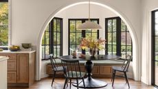 A large kitchen with white walls, wood cabinets, and a large bay window turned into a dining nook with a banquette, round black pedestal table, and black ladder back chairs