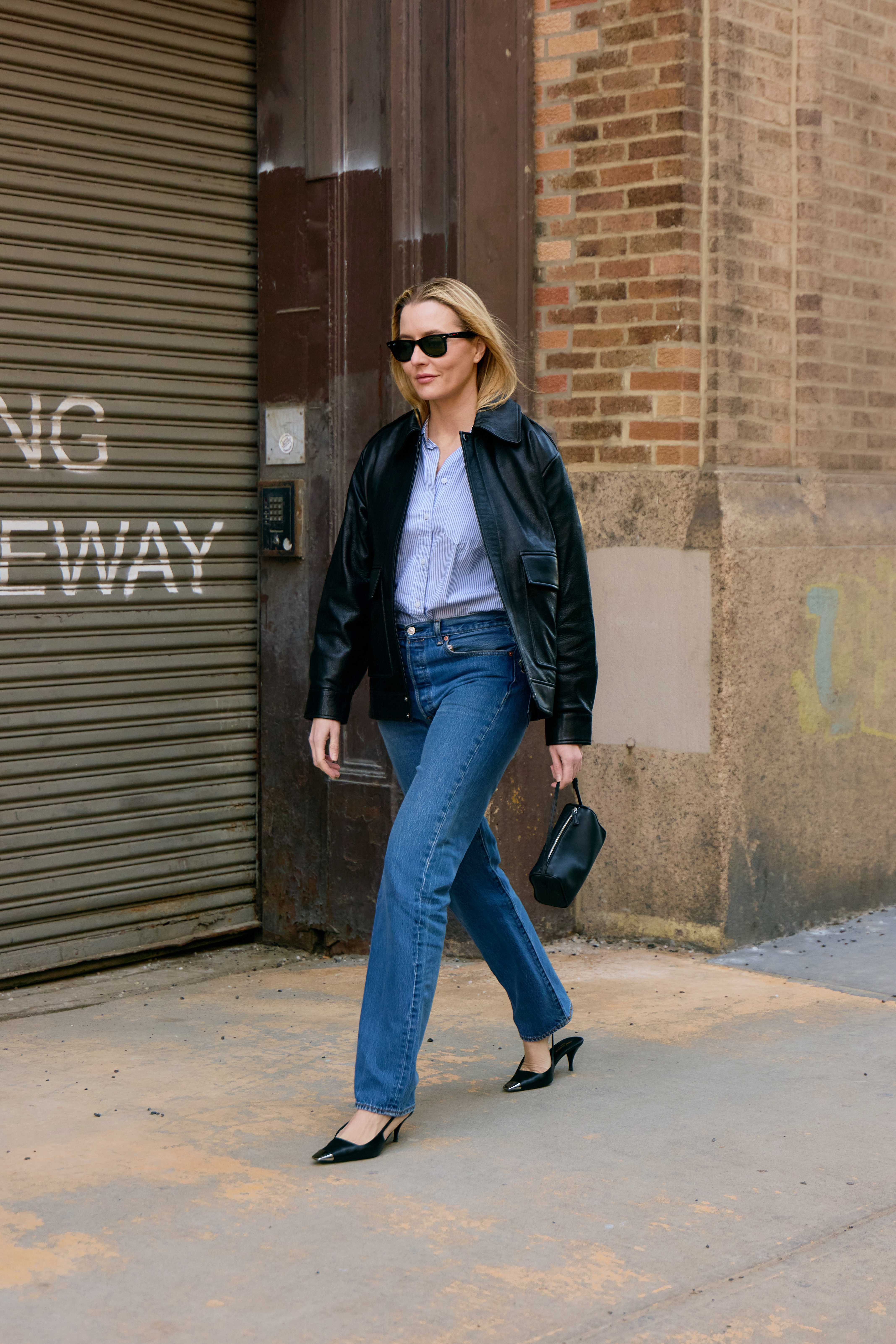 Awoman wearing cigarette jeans, a button-down shirt, and a black leather jacket