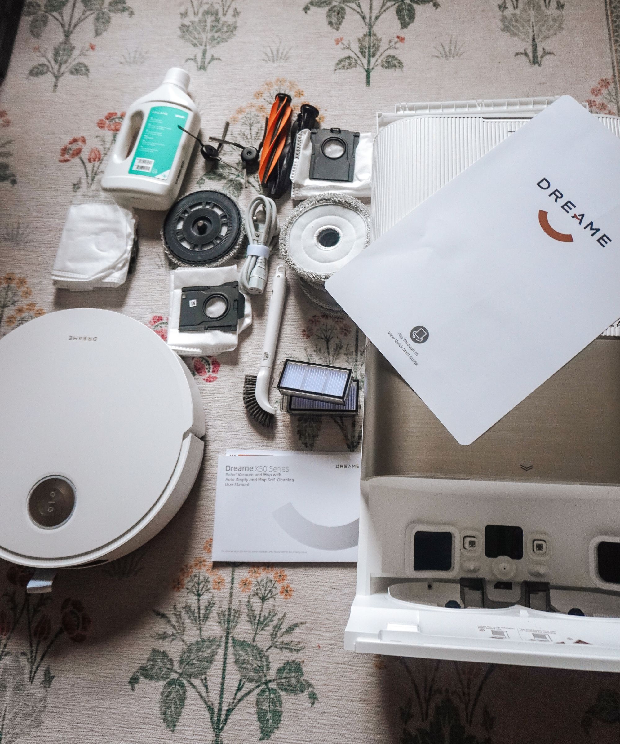The Dreame X50 robot vacuum cleaner with the robot, the base station, the dust bag, and the mop pads on a floral rug