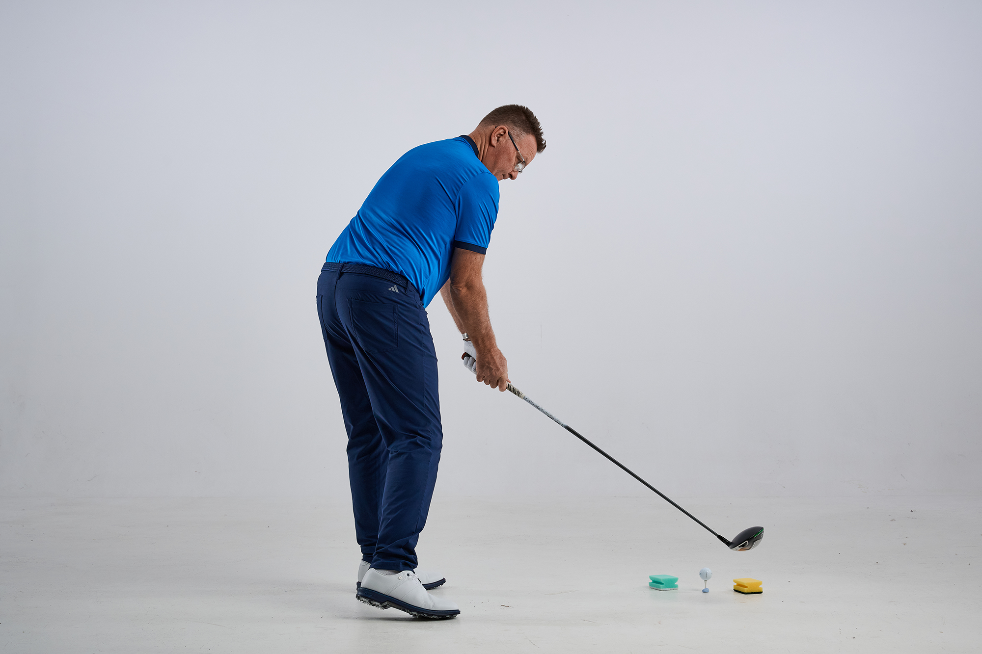 Jon Jacobs demonstrating an over the top swing that causes a slice, with two sponges on the floor that indicate contact with the inside will cause an unwanted left to right shot shape