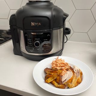 Ninja Foodi 9-in-1 Multi-Cooker behind cooked chicken and potato wedges meal served on a white dinner plate