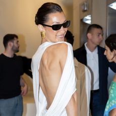 Bella Hadid wears a backless dress by Jacquemus with sunglasses and gold earrings at Cannes