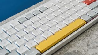 A photo of the NuPhy Air75 V2's yellow space bar and most of its keys, on a stone slab with a blue wall in the background.