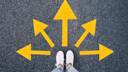 Top view of a person standing on asphalt with yellow arrows pointing in different direction