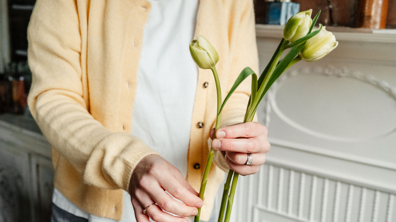Woman in yellow cardigan holding three pale green tupils