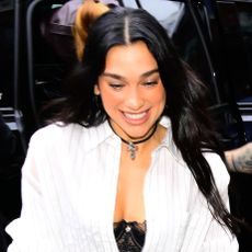 Dua Lipa wearing a striped button-down, gray maxi skirt, and black mesh heels 