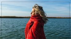 A woman wrapped in a red scarf standing beside water