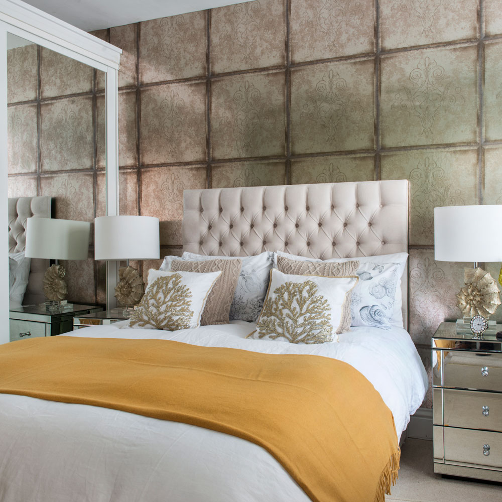 Small bedroom with mirror on cupboard, patterned wallpaper, glass top side tables next to double bed.