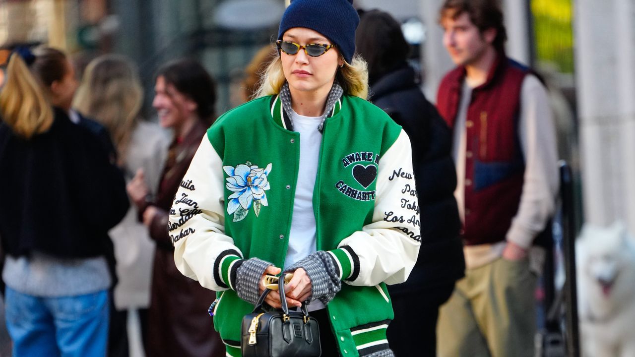 Gigi Hadid in a green varsity jacket, tee shirt, jeans, and a beanie.