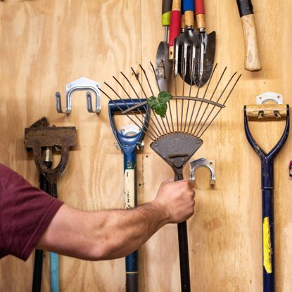 Gardener hanging up rake in shed