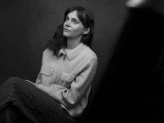 A black and white image of an individual in a photography studio, sat in front of a dark backdrop