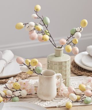 twigs with Easter eggs in a vase and jug on a dining table