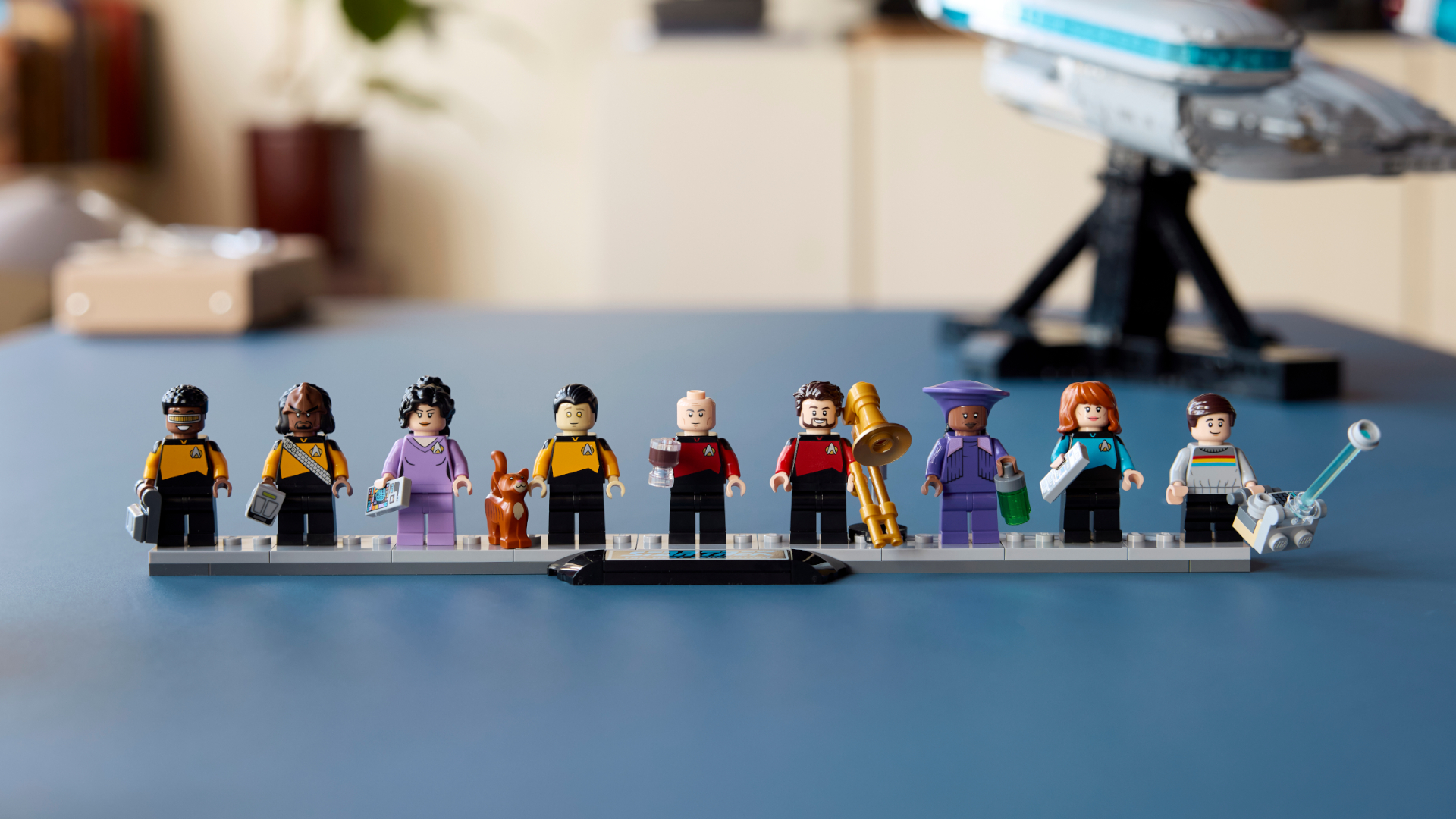 Lego Enterprise minifigures lined up on a stand, in front of the Enterprise set itself
