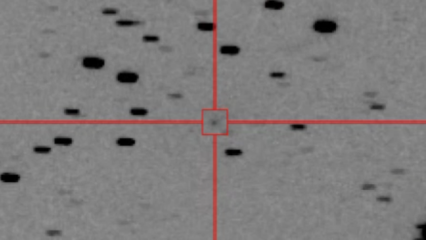 A black and white image shows a gray background speckled with dots with a crosshairs and a box circling a specific dot in the center of the image