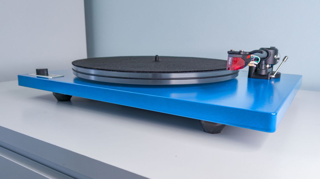 A Blue U-Turn Audio Orbit Special turntable on a white surface, showing the acrylic platter and Ortofon 2M red cartridge