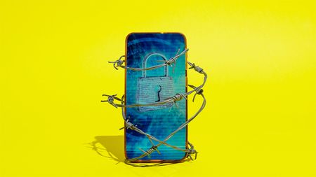 Image of smartphone wrapped in barbed wire. The screen displays a padlock and the phone is in front of a yellow background