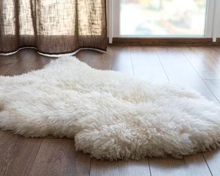 Fish-shaped fluffy white wool rug in middle of wooden floor with light from window in the background