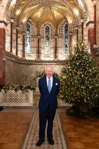 King Charles wearing a blue suit standing in a church in front of a lit Christmas tree