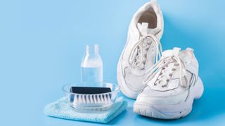 A pair of white sneakers next to a scrubbing brush, cloth and cleaning solution