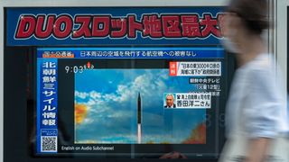 television screen showing a north korean missile flying into the sky, in a store window. person walks past as a blur on the right