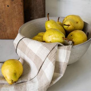 A bowl in a kitchen with pears and a gingham dish cloth