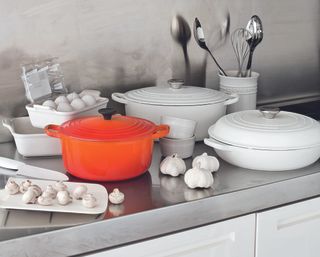 A kitchen countertop covered with cast iron cookware in white and orange