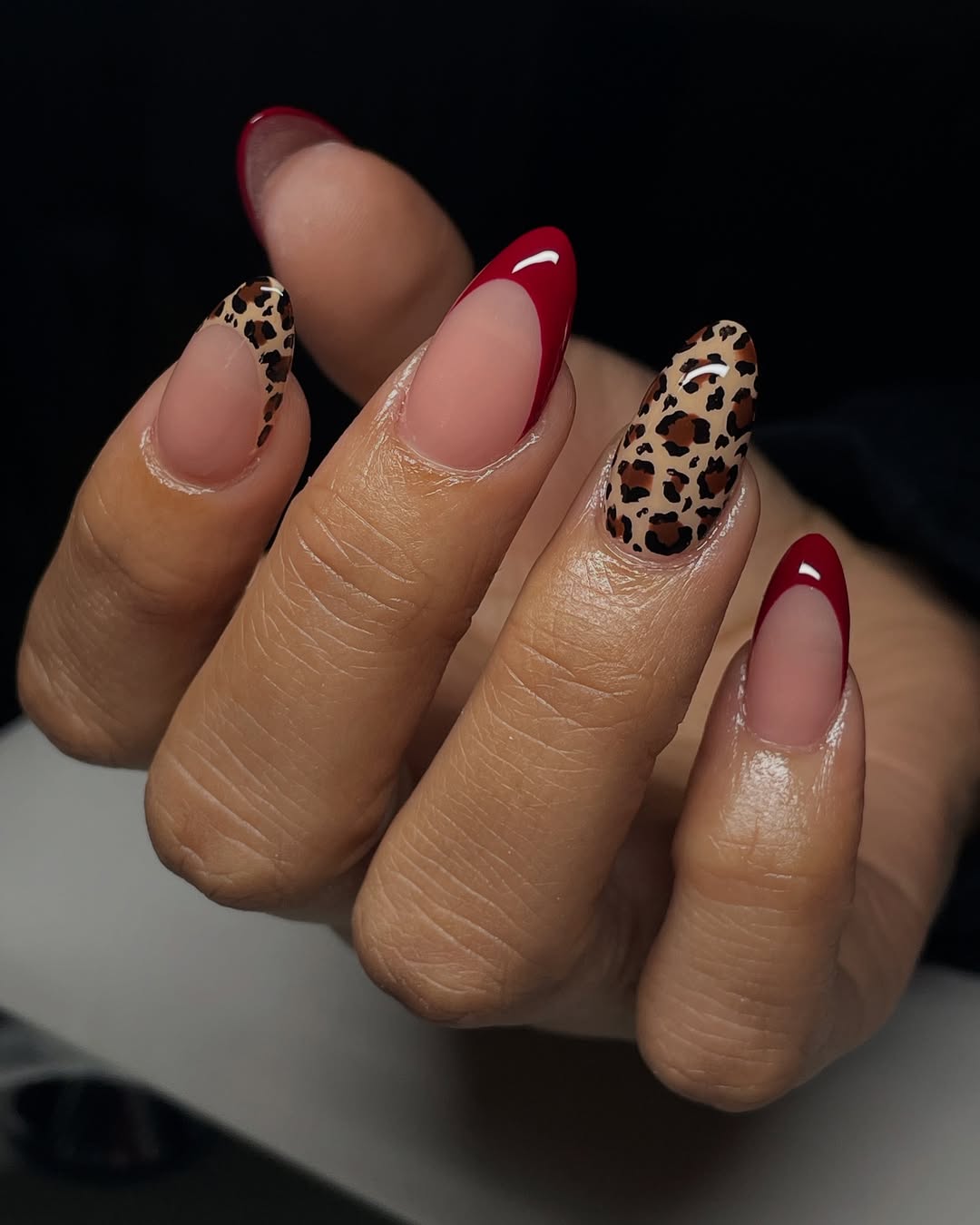 a person wearing leopard nails with red french tips