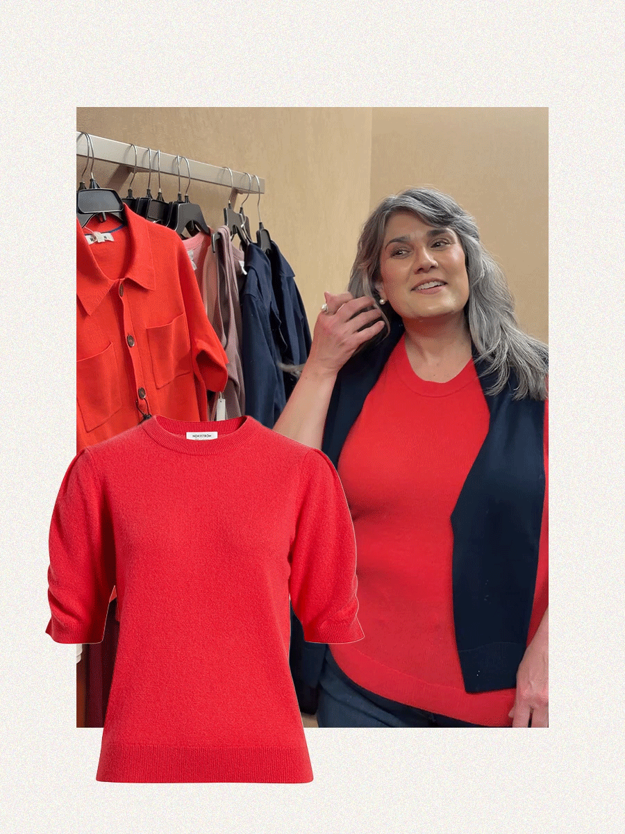 A woman with gray hair trying on a red sweater.