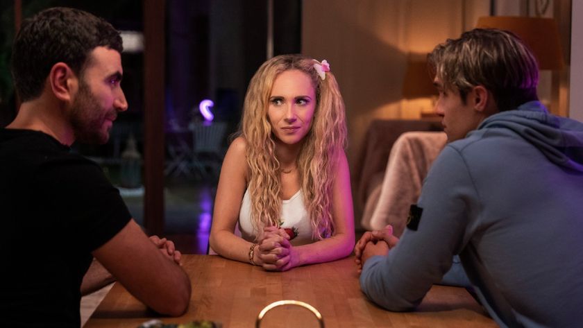 From left to right: the back of Roy, Keeley facing the two boys with her hands on the table looking at Roy, and the back of Jamie.