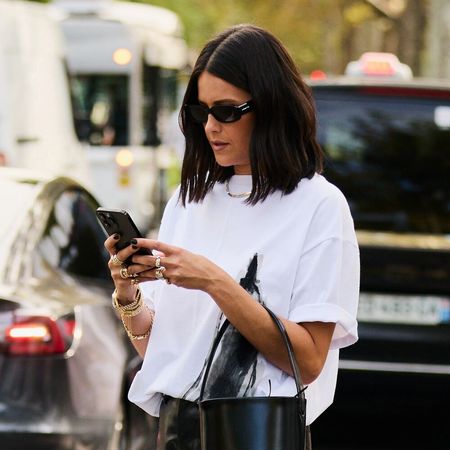 A woman in a white t-shirt and leather pants on her phone
