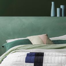 A green bedroom with a contemporary quilt on the bed