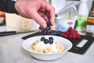 Male cyclist adding blueberries to a bowl of yoghurt and banana