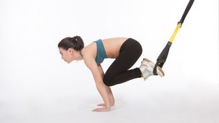 Woman using suspension trainer for knee tucks core exercise with knees drawn in