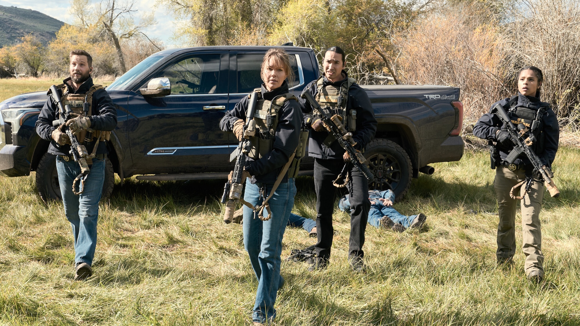 Cal, Belle, Cruz and Miles standing in full uniforms with guns drawn in front of a pickup truck with two men laying on the ground with their arms restrained in Marshals Season 2