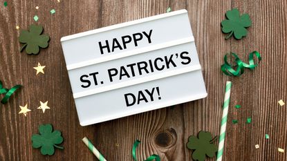 Happy St Patrick's Day in Irish—Lightbox with text. Green clover confetti over brown wooden background. Card for St Patrick's Day with copy space for text.