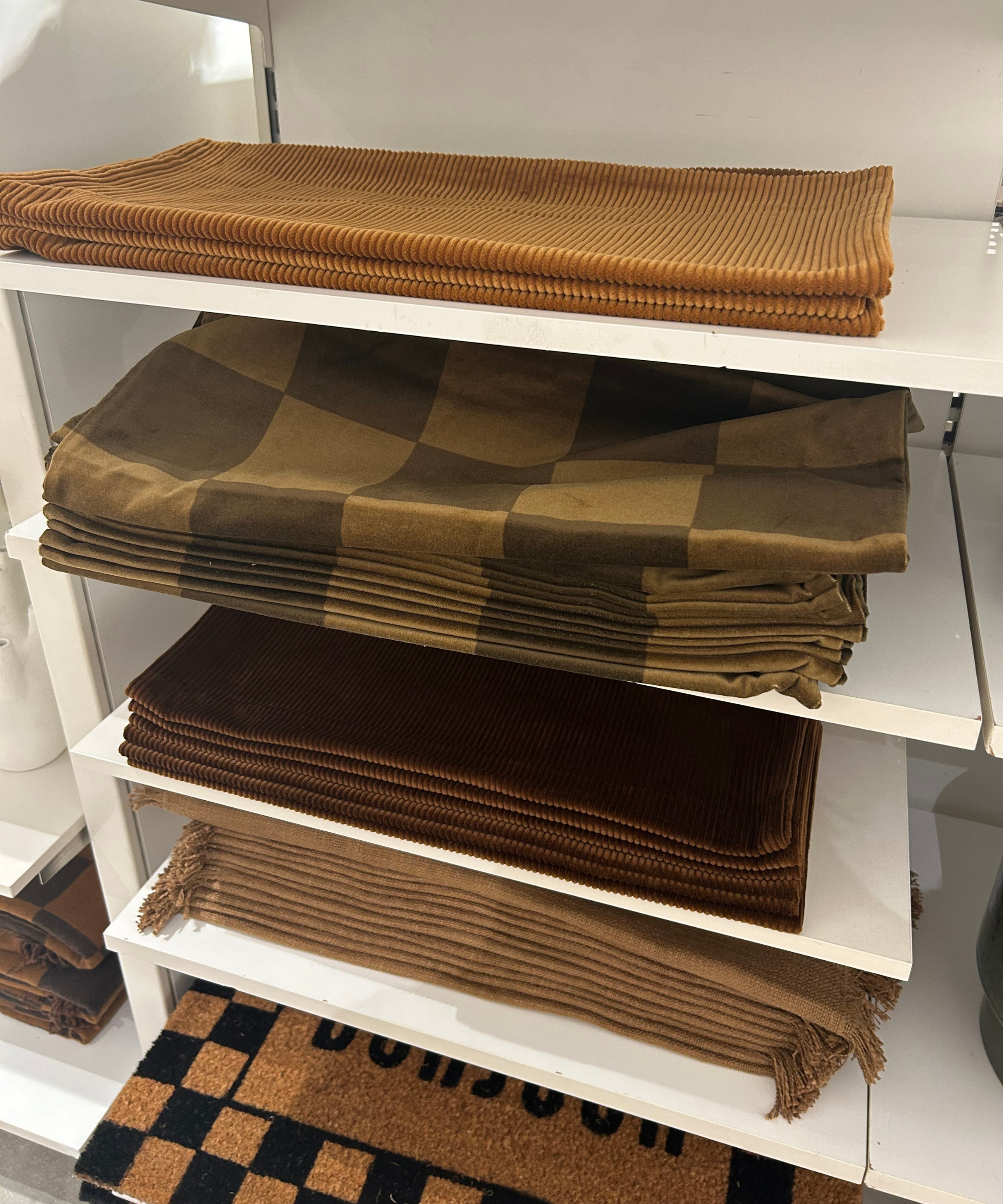 a shelving unit holding a collection of pillow covers in varying shades of green and brown