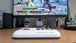 Hori Fighting Stick Mini placed on desk surface with monitor playing Street Fighter 6 in the background