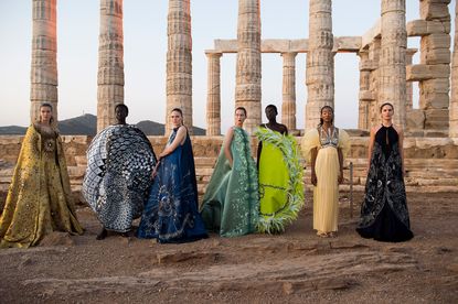 Row of women pose for picture in front of structures