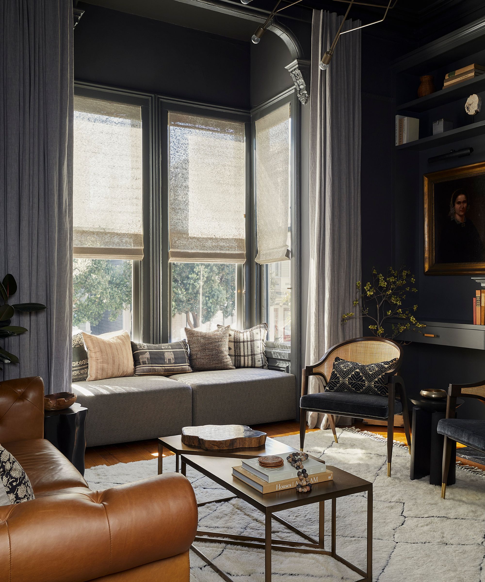 Dark, moody living room with a brown leather sofa, window seat, and woven chair