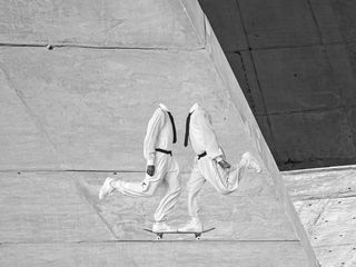 Black and white image of two headless people standing on one leg on the same skateboard