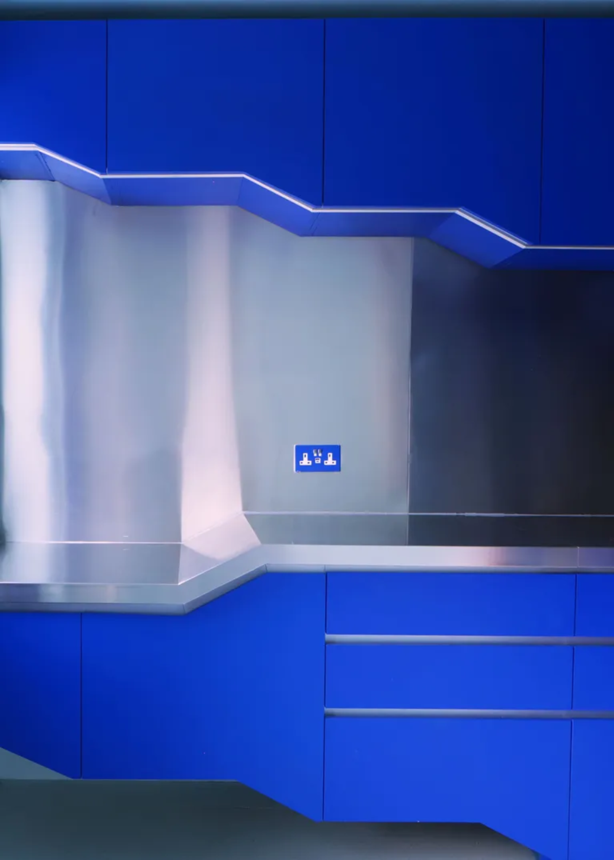An industrial-style kitchen with chrome counters and cobalt blue cabinets and drawers